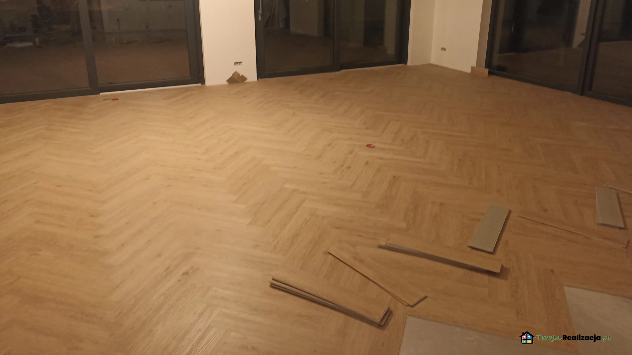 Rzemieślnik układa panele w jodełkę na podłodze salonu, precyzyjnie dopasowując kolejne elementy