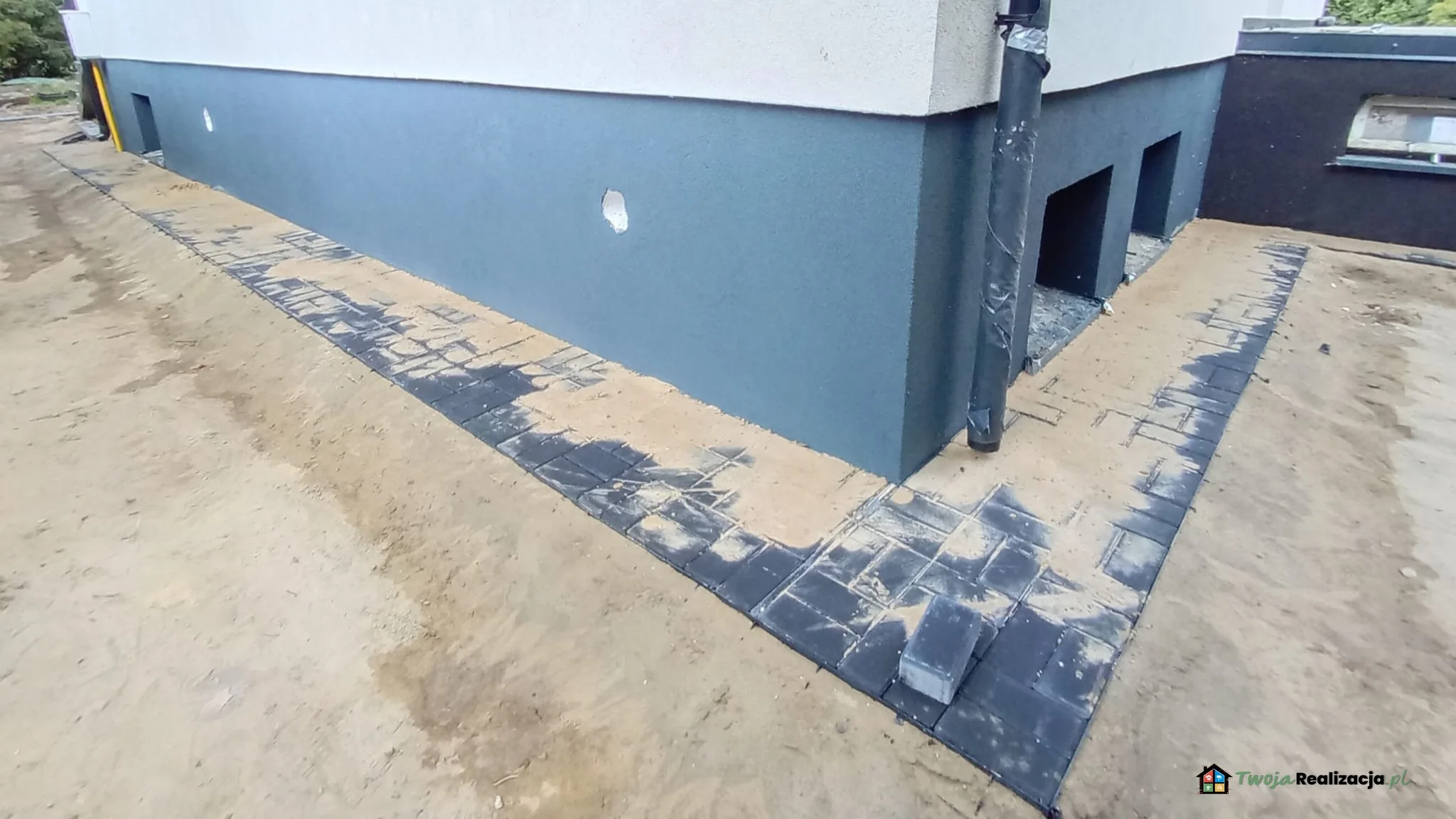 Ocieplenie ściany fundamentowej piwnicy w domu jednorodzinnym pod Łodzią Płyty izolacyjne przyklejone do ściany fundamentowej piwnicy domu jednorodzinnego podczas prac ociepleniowych pod Łodzią